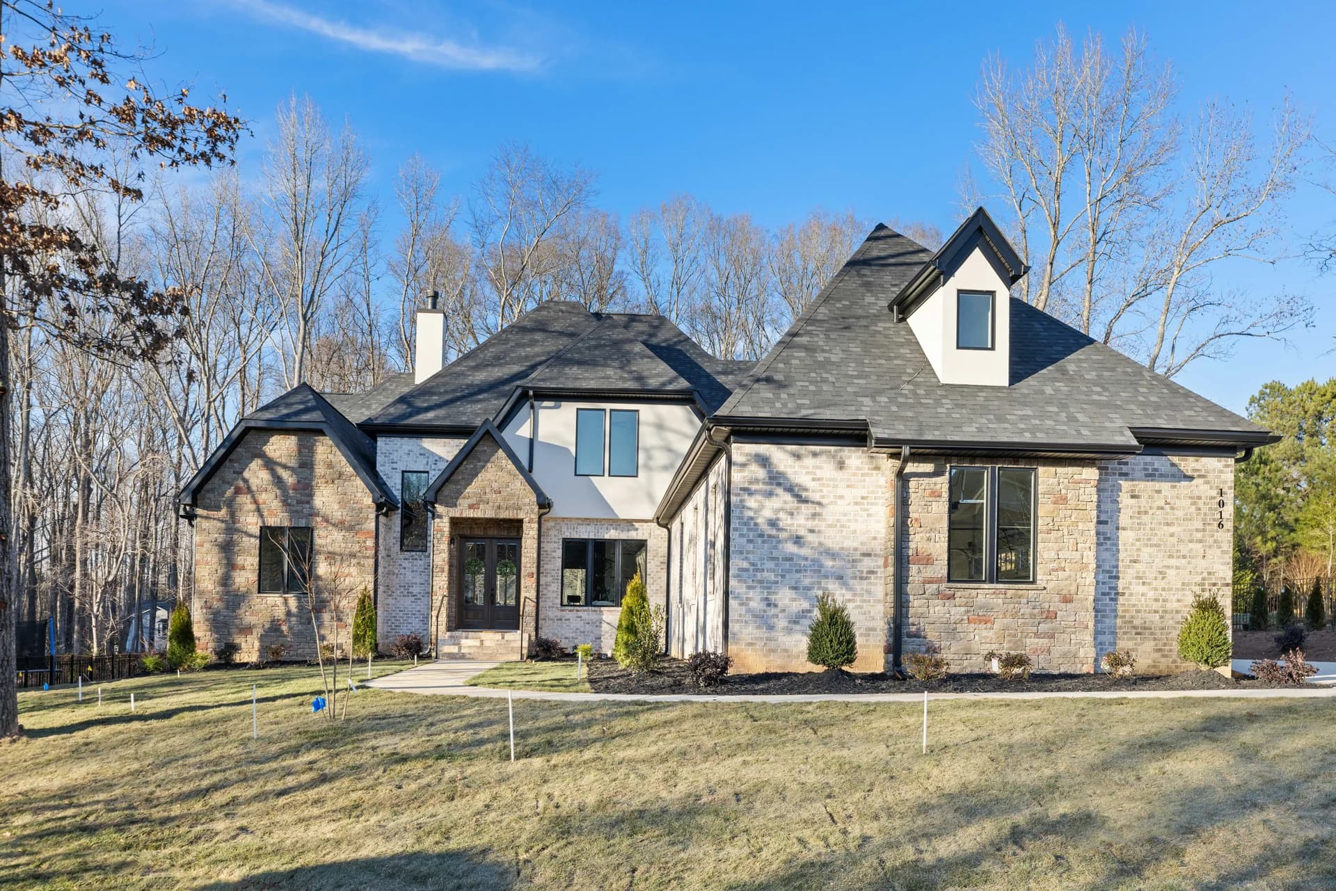 Stone and brick home with dark rooflines and a covered entry at Sherringham Way